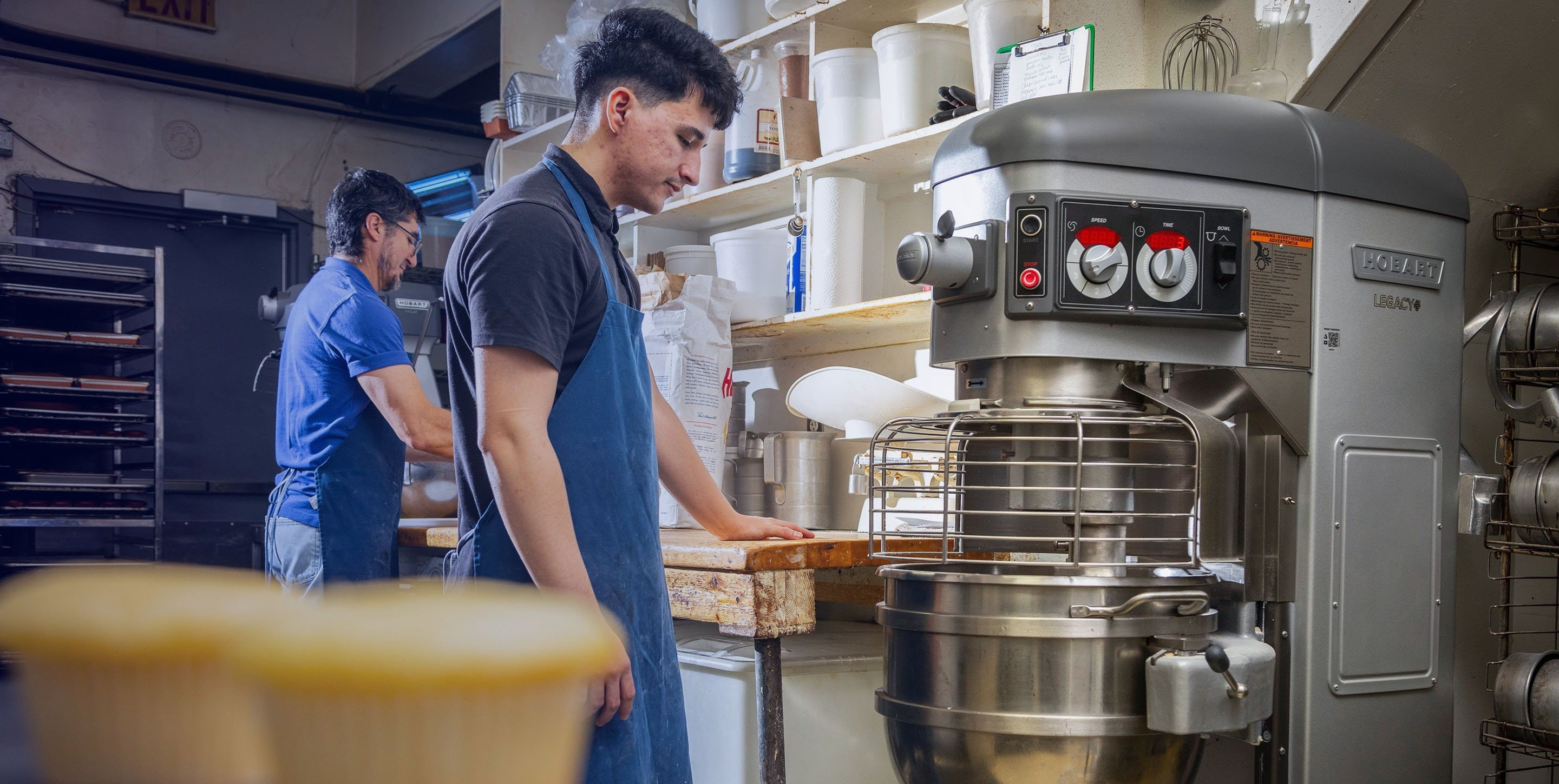 Baker operating a Hobart Legacy Plus heavy-duty mixer in a commercial kitchen.